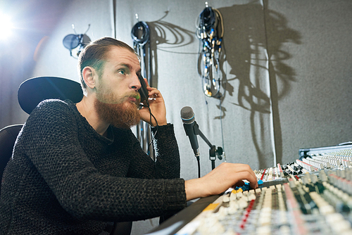 Side view of confident bearded man using music board and earphones working in sound studio.
