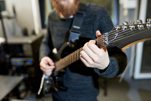 Close-up of unrecognizable hipster musician composing new melody while playing electric guitar and holding fingers on fretboard of musical instrument in studio