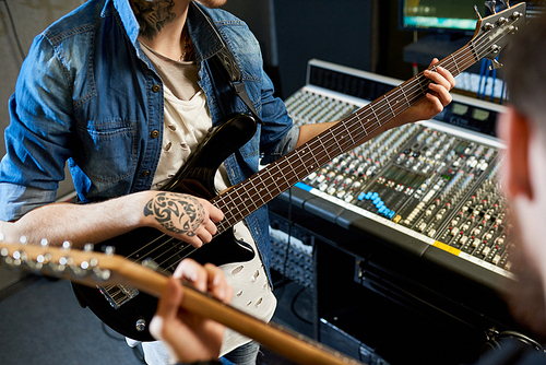 Crop shot of modern performers playing guitars in sound studio while collaborating new song.