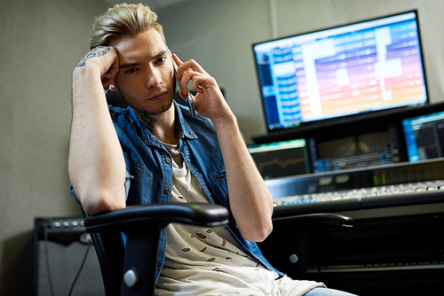 Trendy man having phone call while working at board in music recording studio.