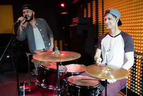 Portrait of modern hip-hop singer performing with his band in recording studio, drummer in foreground