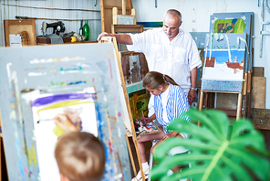 Portrait of senior  art teacher watching children painting during art class in school