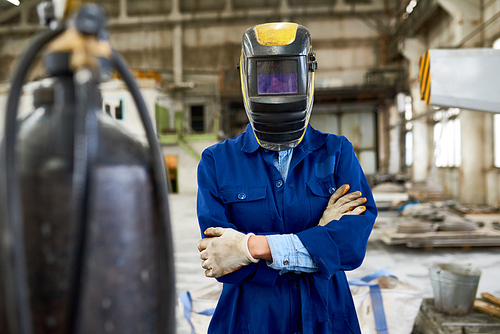 Portrait of young woman wearing welding mask standing posing confidently with arms crossed in industrial workshop of modern factory