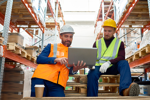 Portrait of two factory workers using laptop on break in warehouse, copy space