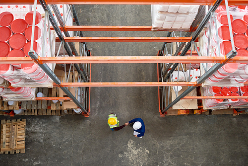 Top view background image of tall shelves in modern warehouse with two workers wearing hardhats shaking hands standing in aisle