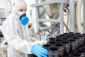 Sports nutrition production worker in protective clothing taking empty container from stack.