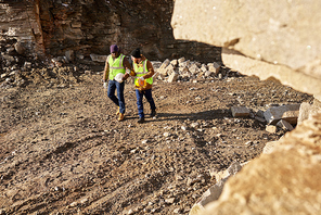 High angle shot of two industrial  workers wearing reflective jackets walking in dirt on mining worksite outdoors, copy space