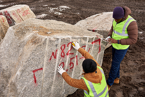 High angle of two industrial workers wearing reflective jacket marking  granite on mining worksite, copy space