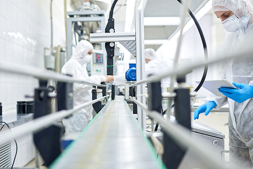 Sports nutrition production employees working in protective clothing at conveyor belt.