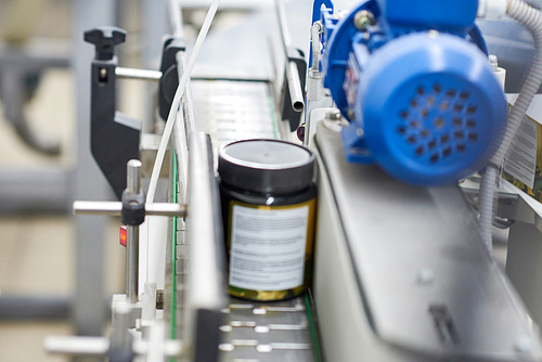 Close-up shot of pill bottle moving along conveyor line of modern pharmaceutical factory, blurred background