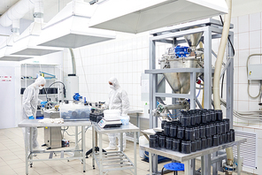 Team of highly professional factory workers wearing coveralls and safety masks taking inventory in warehouse of pharmaceutical factory