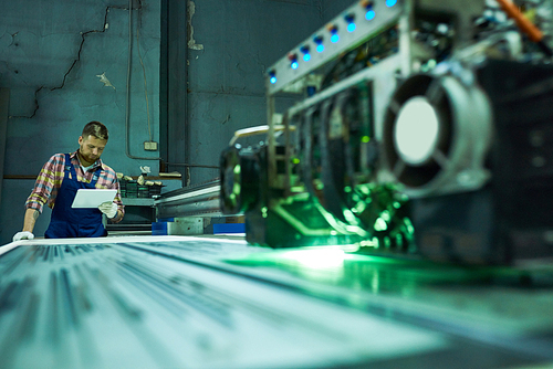 Portrait of young factory worker operating modern laser engraving equipment in industrial workshop, copy space