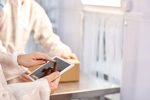 Crop close-up worker hands using tablet computer at sports nutrition production.