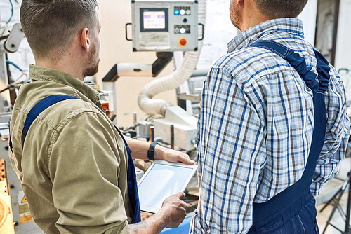 Back view portrait of two factory workers using modern machine at factory operating it via digital tablet, copy space