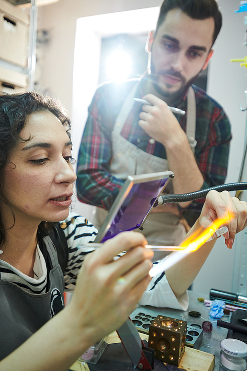 Portrait of creative young woman shaping glass over gas torch while making beads for handmade jewelry in glassworking studio, copy space