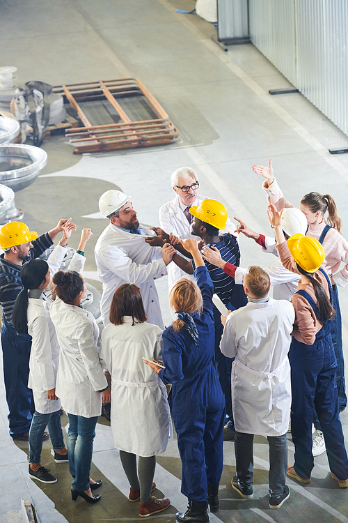 Group of angry factory workers attacking business executives during strike meeting in industrial workshop