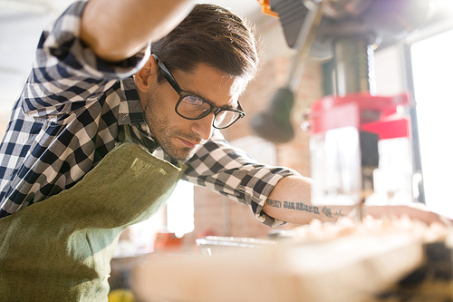 Low angle portrait of handsome modern artisan using machines while working  with wood in carpenters shop