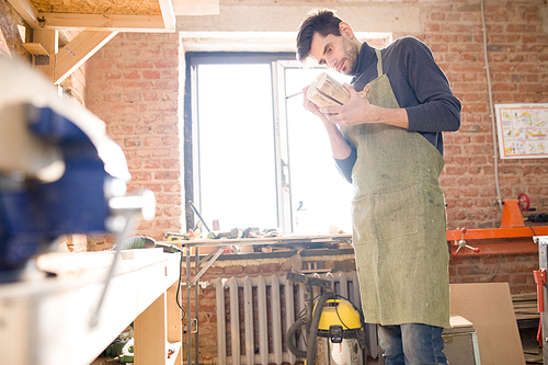 Low angle portrait of  modern artisan holding piece of wood and marking it while  in carpenters shop, copy space