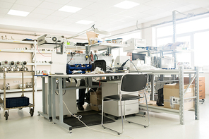 Interior of modern production department of manometer factory: engineers wearing lab coat sitting at desks, panoramic windows, table trolley with pressure sensors