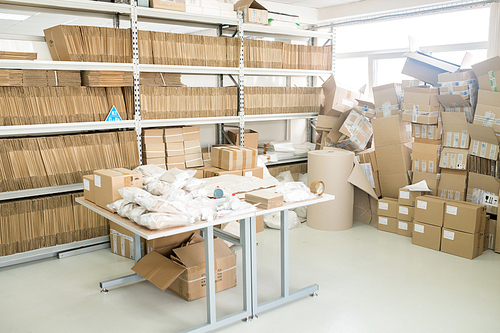 Interior of spacious warehouse of measuring equipment factory: piles of cardboard boxes, adhesive tapes and wrapping paper roll