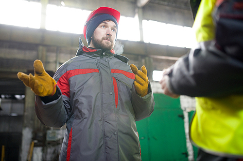 Waist up portrait of modern bearded worker  wearing warm jacket and hardhat discussing production with foreman  in workshop
