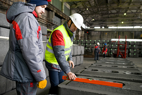 Side view portrait of two workers measuring concrete blocks while doing quality control in workshop of industrial plant, copy space