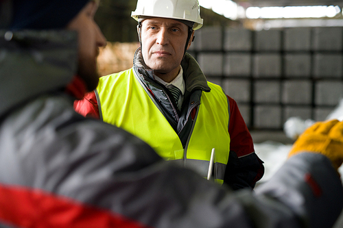 Waist up portrait of mature foreman wearing hardhat  discussing manufacturing with worker while standing in workshop