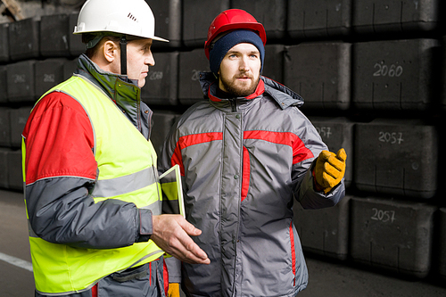 Waist up portrait of factory worker wearing hardhat  taking to foreman while standing in workshop