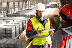 Waist up portrait of mature factory foreman wearing hardhat talking to worker at industrial factory, copy space