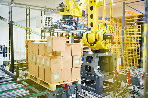 Automatic packaging machine working upon pile of cardboard boxes, interior of spacious warehouse on background