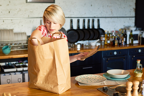 Young woman with paper bag and product list on the kitchen