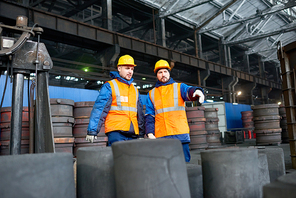 Group of concentrated workers wearing reflective vests and hardhats standing at production department of modern plant and counting made details