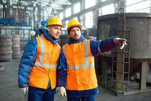 Handsome young worker wearing uniform and protective helmet listening to his superior with concentration while standing at production department of modern plant