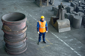 High angle view of pensive bearded worker wearing uniform and protective helmet standing at spacious department of modern plant and looking away