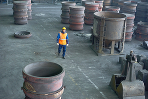 High angle view of bearded engineer wearing uniform and protective helmet walking along production department of modern plant