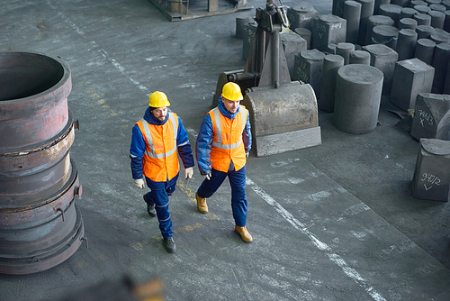High angle view of two bearded technicians wearing uniform and hardhats walking along production department of modern plant