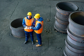 High angle view of two concentrated workers wearing uniform and hardhats standing at spacious production department of modern plant and taking notes while carrying out inventory.