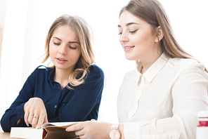 Female students sitting together at the table and reading a book