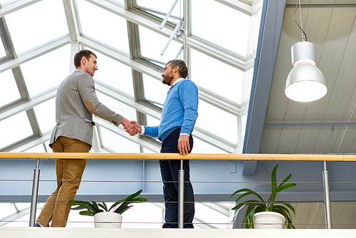 Full length  portrait of two successful business men standing on balcony in modern office building and shaking hands, copy space