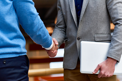 Mid-section close up of two successful modern businessmen shaking hands in office building, business deal concept