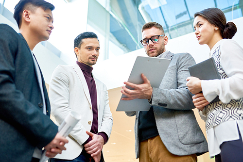 Low angle view at group of successful business people discussing work while standing in circle in modern office building