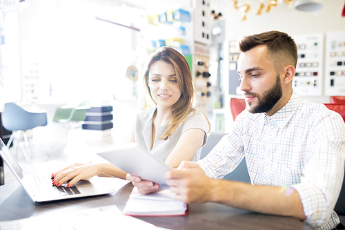 Portrait of two managers, man and woman, sitting at desk in sunlit store and planning work, copy space