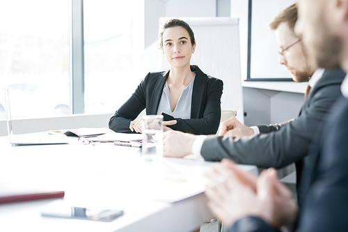 Group of young entrepreneurs sitting at meeting table in conference room and discussing startup projects, focus on smiling businesswoman listening to colleagues, copy space