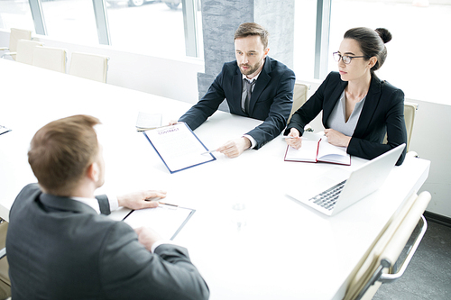 Portrait of three successful business people, man and woman,  talking to partner sitting across meeting table in conference room, copy space