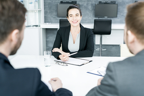 Portrait of smiling businesswoman heading meeting listening to partners sitting across table in conference room, copy space