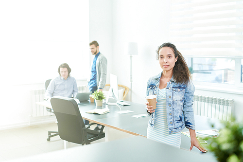 Serious calm confident young Hispanic businesswoman in stylish outfit drinking coffee and  in modern office