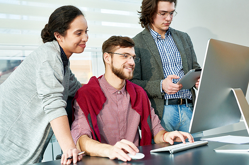 Group of young male and female managers smiling cheerfully while having video chat with colleagues on computer