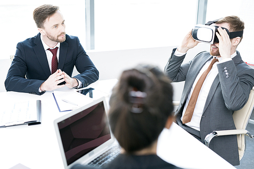 Portrait of contemporary businessman enjoying  VR while sitting at meeting table in conference room, copy space