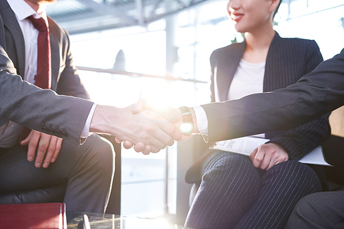 Close-up shot of business partners shaking hands after successful completion of important negotiations, lens flare