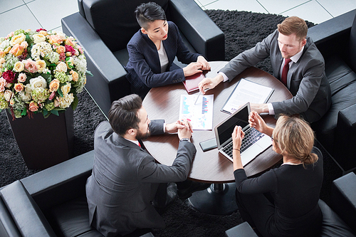 Working process at modern boardroom: group of hard-working managers in formalwear sitting at table and discussing faced issue with each other, high angle view